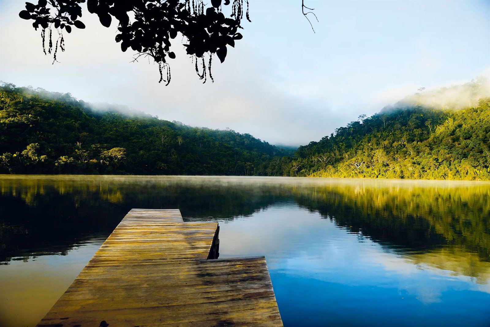 Muelle de madera sobre la Laguna Azul al amanecer, rodeada de selva